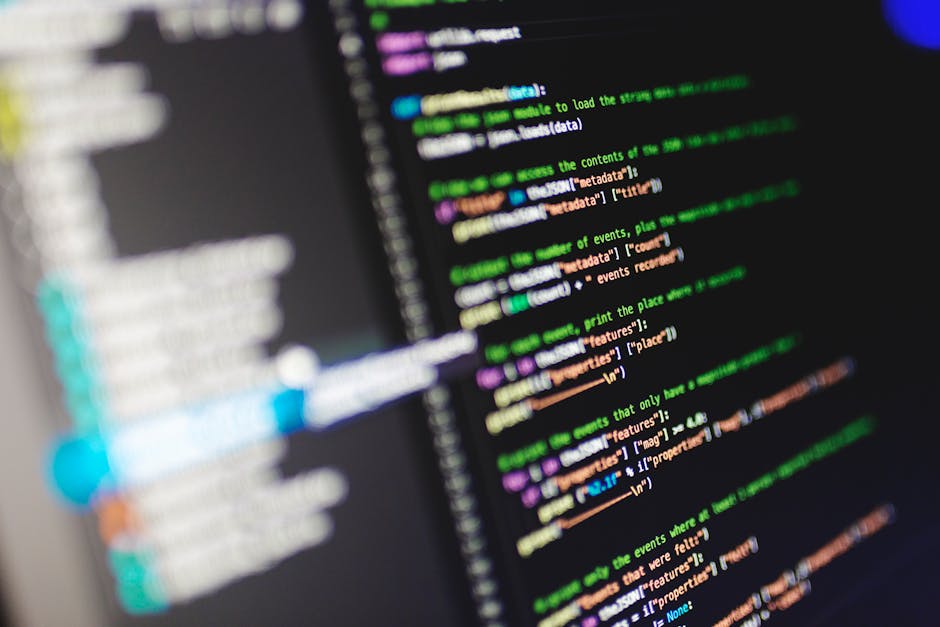 Close-up image of a computer screen displaying lines of colorful code on a black background, with syntax highlighting in shades of green, purple, orange, and blue. The code appears to be programming t