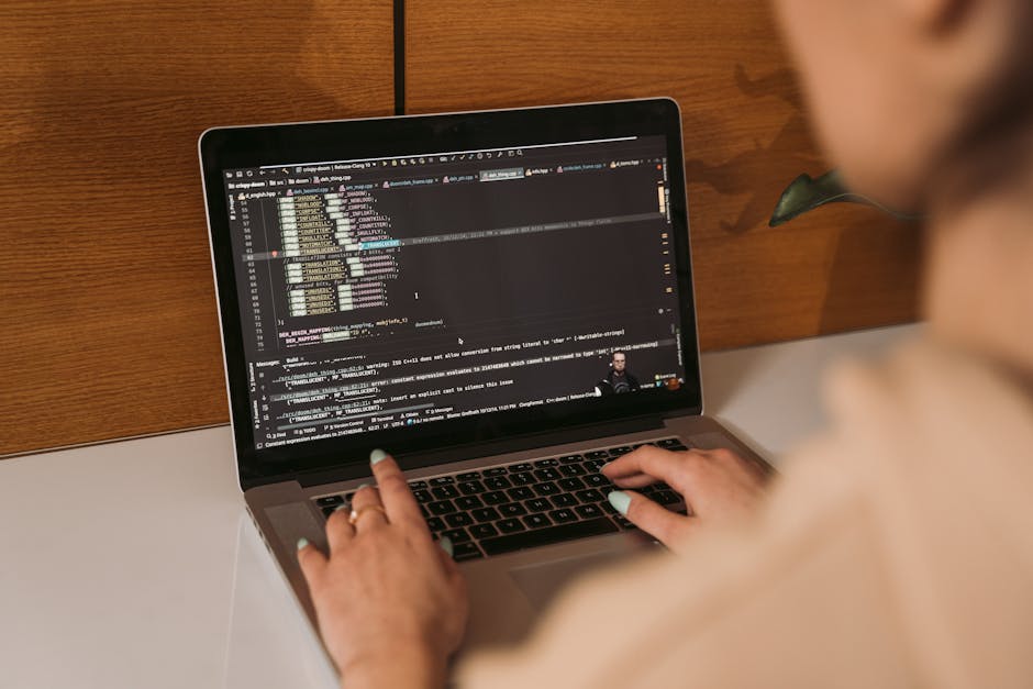 Close-up image of a computer screen displaying lines of colorful code on a black background, with syntax highlighting in shades of green, purple, orange, and blue. The code appears to be programming t